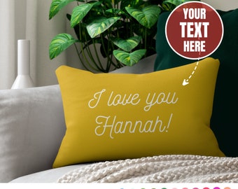 May include: A yellow throw pillow with the text "I love you Hannah!" in white cursive font. The pillow is on a couch with a green throw blanket and a plant in the background. The image also includes a red circle with the text "YOUR TEXT HERE" in white.