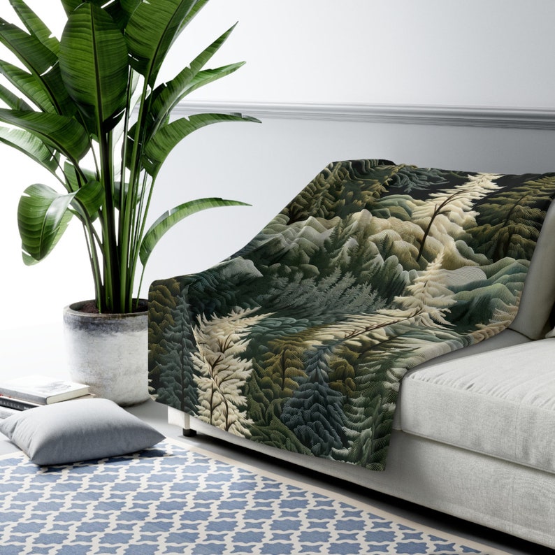 May include: A soft, green and white throw blanket with a forest scene design. The blanket is draped over a white couch.