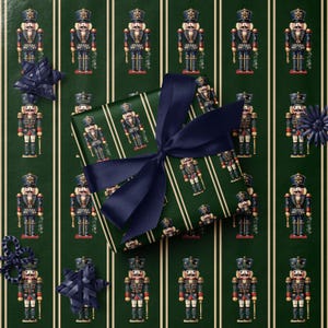 May include: A wrapped gift with a navy blue bow sits on a green background with vertical white stripes. The wrapping paper and background feature a repeating pattern of nutcracker soldiers in red, blue, and gold. Decorative navy blue stars and a flower are also present.