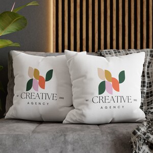 Pode incluir: Duas almofadas brancas com um design geom&eacute;trico em tons de rosa, laranja, amarelo e verde. As almofadas t&ecirc;m o texto "NY CREATIVE 2002 AGENCY" impresso nelas.