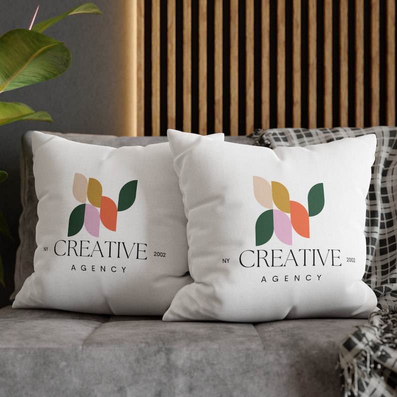 Pode incluir: Duas almofadas brancas com um design geom&eacute;trico em tons de rosa, laranja, amarelo e verde. As almofadas t&ecirc;m o texto "NY CREATIVE 2002 AGENCY" impresso nelas.