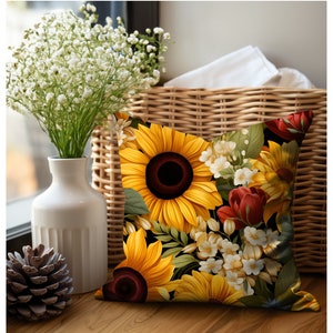 Puede incluir: Una almohada de tiro con un dise&ntilde;o floral que presenta girasoles, flores rojas y flores blancas sobre un fondo negro.