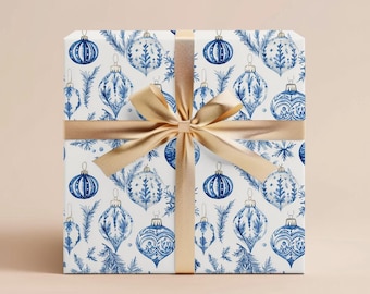 May include: A white gift box with a blue and gold pattern of Christmas ornaments and pine branches. The box is tied with a gold ribbon.