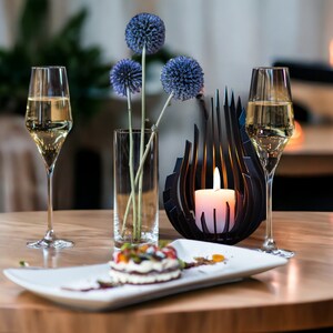 May include: A table setting with two glasses of white wine, a plate with a dessert, a vase with blue flowers, and a candle holder with a lit candle.