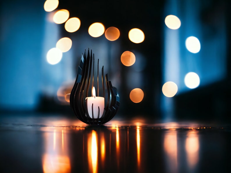 May include: A black metal candle holder shaped like a flame with a white candle inside. The candle holder is on a dark surface with a blurry background of warm white lights.