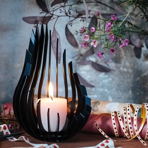 May include: A black metal candle holder shaped like a flame with a white candle inside. The candle holder is sitting on a table with pink and white ribbon and a pair of scissors.