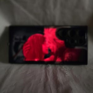 May include: A close-up of a black rectangular frame with a red and white image inside. The image is blurry and appears to be of a person.