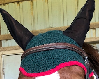 May include: A green and red horse fly bonnet with black mesh ear covers. The bonnet is made of a crocheted material and has a brown leather strap.