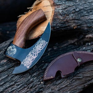 May include: A black and silver axe with a wooden handle and a leather sheath. The axe has a decorative design on the blade.
