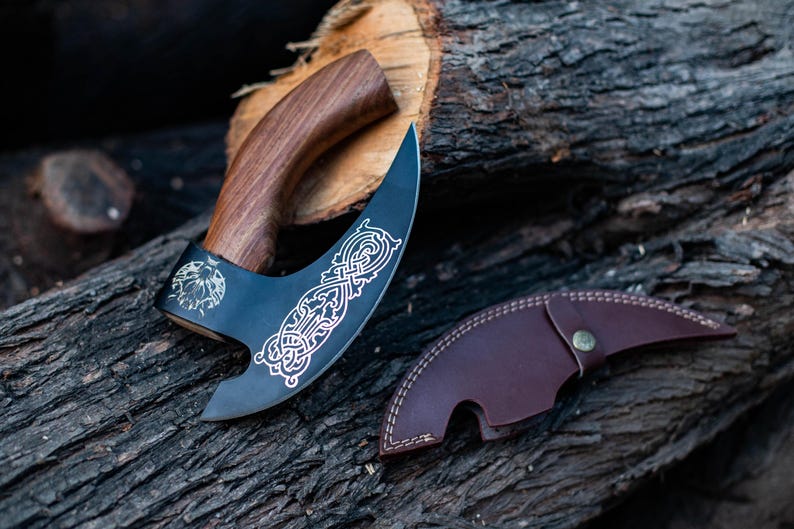 May include: A black and silver axe with a wooden handle and a leather sheath. The axe has a decorative design on the blade.