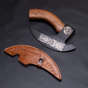 May include: A black and silver axe with a wooden handle and a leather sheath. The axe has an intricate design on the blade.