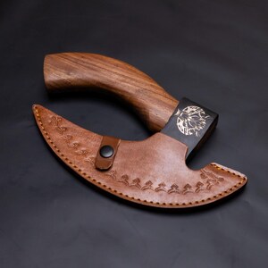 May include: A brown wooden handled axe with a black metal head and a brown leather sheath. The sheath has a floral design and a snap closure.