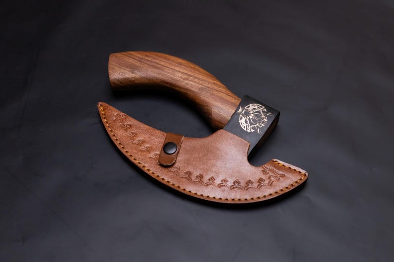 May include: A brown wooden handled axe with a black metal head and a brown leather sheath. The sheath has a floral design and a snap closure.