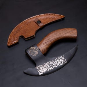 May include: A black and silver axe with a wooden handle and a leather sheath. The axe blade has an intricate design.