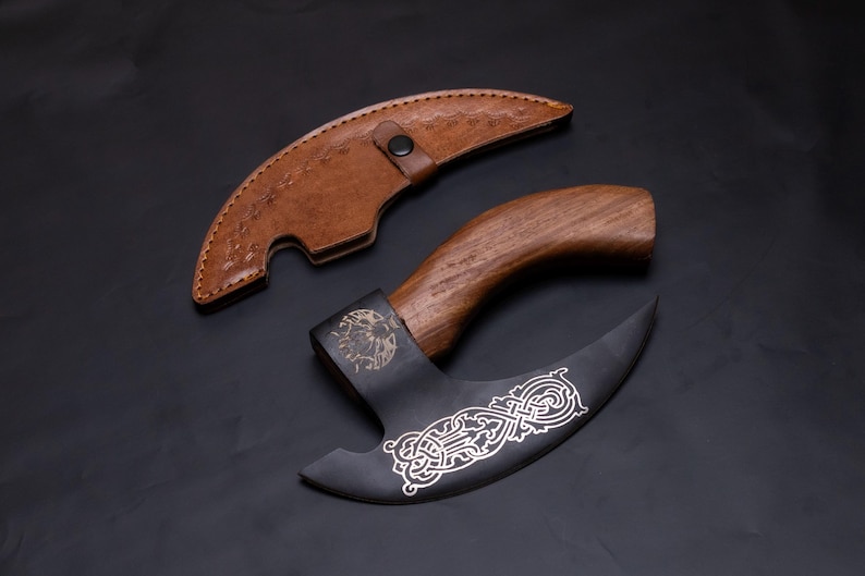 May include: A black and silver axe with a wooden handle and a leather sheath. The axe blade has an intricate design.