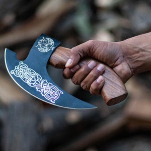 May include: A black axe with a wooden handle and a silver design. The axe has a curved blade and a decorative pattern on the blade.