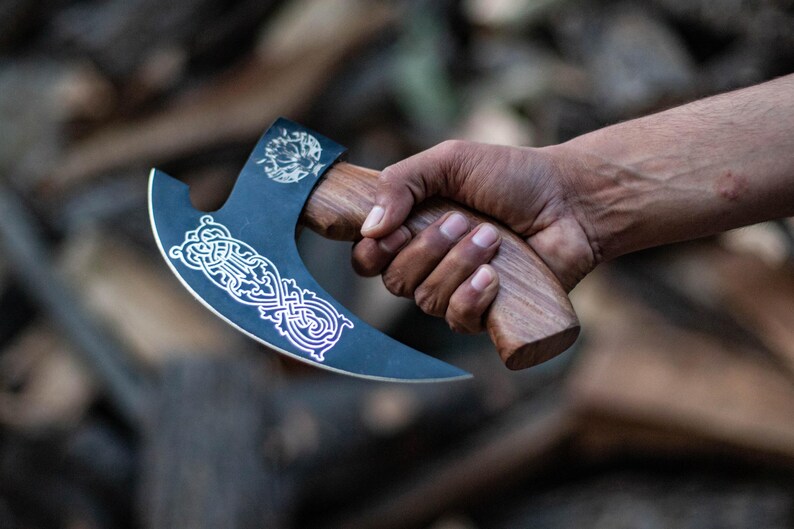May include: A black axe with a wooden handle and a silver design. The axe has a curved blade and a decorative pattern on the blade.