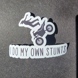 Puede incluir: Una pegatina blanca con una silueta negra de una persona haciendo una acrobacia en una moto de cross. El texto "I DO MY OWN STUNTS" está escrito en negro en la pegatina.