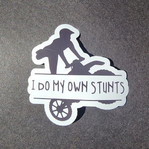 Op de afbeelding: Witte sticker met een silhouet van een persoon die een stunt uitvoert op een crossmotor. De tekst "I do my own stunts" staat op de sticker.