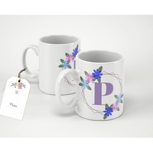 Può includere: Due tazze in ceramica bianca con un design floreale e una lettera "P" di colore viola. Le tazze sono su una superficie bianca. Una tazza ha un'etichetta regalo con le parole "A :" e "Da :" su di essa.