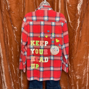 May include: Red and white plaid flannel shirt with the words "KEEP YOUR HEAD UP" in colorful felt letters and a smiling face appliqué.