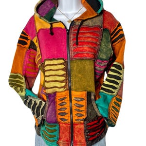 May include: A patchwork hoodie with a full-length zipper, featuring a vibrant mix of colors including pink, orange, green, and purple. The jacket has a hood and pockets, with decorative cut-out details. The garment is displayed on a mannequin.