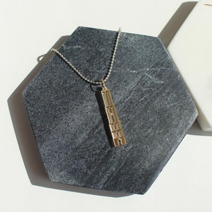 Op de afbeelding: Een gouden ketting- en oorstekerset met een gedetailleerd gebouwpendulum. De ketting is aan een zilveren ketting en de oorbellen zijn van het hangende type.