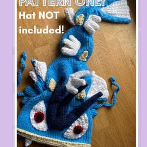 Może przedstawiać: Szydełkowy niebieski kapelusz z białymi i beżowymi detalami, zaprojektowany z dużymi oczami, płetwami i rogami. Widoczny jest tekst "PATTERN ONLY Hat NOT included!". Kapelusz jest prawdopodobnie częścią kostiumu lub cosplayu.