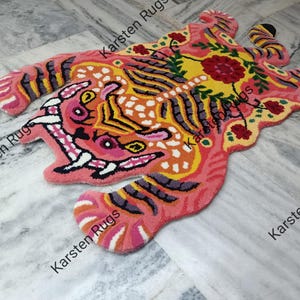May include: A pink, yellow, and orange tiger rug with black stripes. The rug has a floral design with red and green accents.
