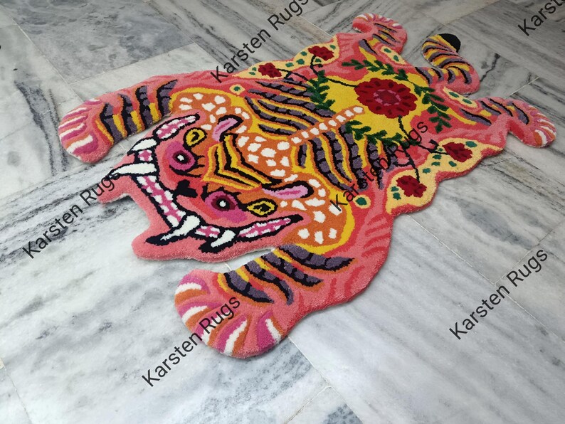 May include: A pink, yellow, and orange tiger rug with black stripes. The rug has a floral design with red and green accents.