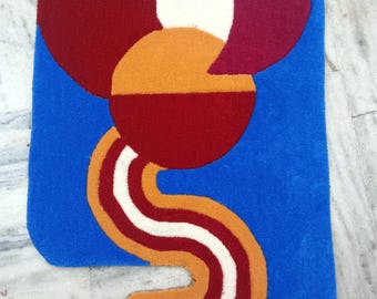 May include: A blue, red, white, and orange abstract rug with a curved design. The rug has a geometric pattern and is made of soft, plush fibers.