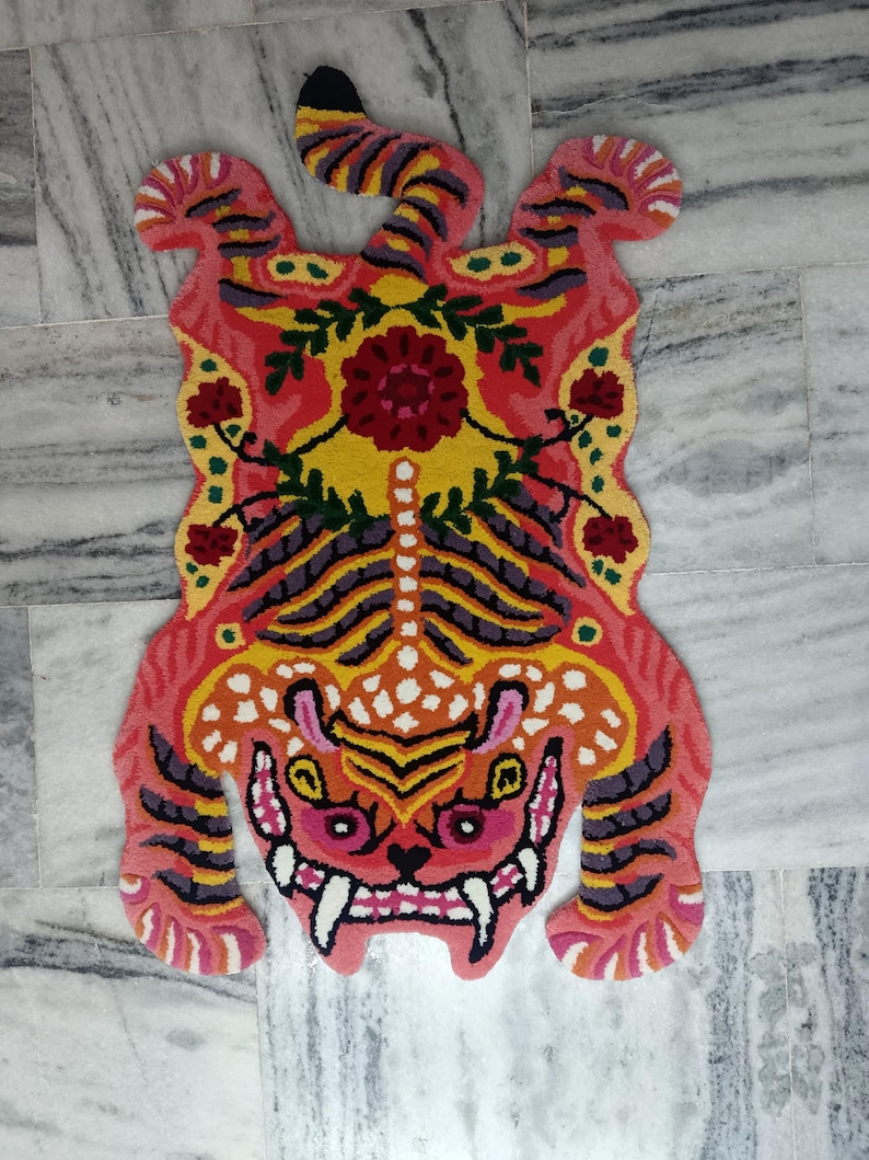 May include: A pink and yellow tiger rug with floral details. The rug is made of a soft, plush material and features a detailed tiger face with fangs.