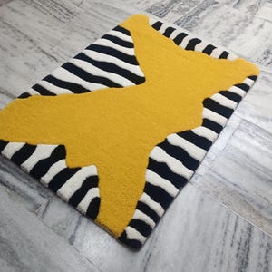Puede incluir: Una alfombra rayada en negro y amarillo con una gran forma de mariposa amarilla en el centro.