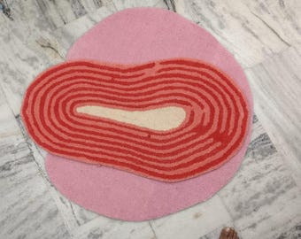 May include: A pink and red patterned rug with a unique, organic shape. The rug has a layered design with a red center and a pink outer layer.