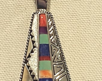 May include: A silver pendant necklace with a triangular shaped pendant featuring a geometric design and inlaid turquoise, coral, and lapis lazuli stones.