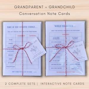 May include: Two sets of white interactive note cards titled GRANDPARENT + GRANDCHILD Conversation Note Cards, wrapped in red and white twine with attached tags. The cards feature blue text, grids for filling out favorite things, and would you rather questions.