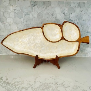 May include: A wooden leaf-shaped serving tray with a mother-of-pearl inlay. The tray has three circular compartments and a larger, leaf-shaped section. It is supported by a small, wooden stand. The tray is approximately 50 cm long.