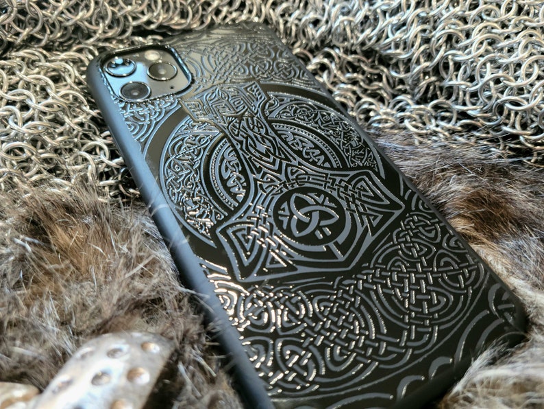 May include: Black phone case with a detailed, embossed design of a Celtic knot and a hammer. The design is in a silver color.