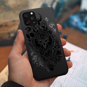 Puede incluir: Carcasa de tel&eacute;fono negra con un dise&ntilde;o detallado de un &aacute;rbol con ramas, hojas y animales. El dise&ntilde;o es de color gris oscuro y tiene un aspecto texturizado.