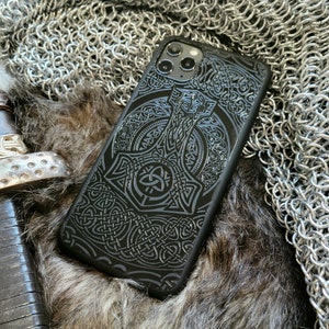 May include: Black phone case with a detailed design of a hammer and intricate knotwork. The case has a raised camera bump with three lenses.