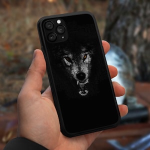 May include: Black phone case featuring a white wolf face graphic. The wolf's eyes are yellow and it is snarling.