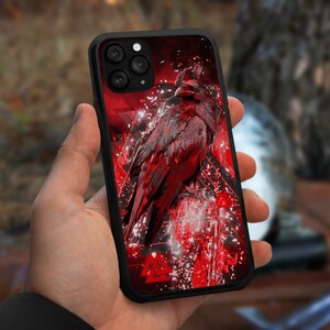 May include: A black phone case with a red and white design featuring a raven with a black and red color scheme. The case has a camera cutout and a geometric pattern.