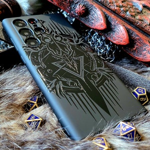 May include: A black phone case with a detailed design of a sword and other fantasy elements. The case is lying on a furry surface with blue and gold dice.