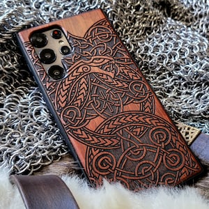 Könnte beinhalten: Eine Handyhülle aus Holz mit einer detaillierten Schnitzerei eines keltischen Knotenmusters in Braun und Schwarz. Die Hülle ist für ein Smartphone mit einem dreifachen Kameraobjektiv konzipiert.
