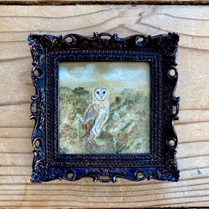 Peut inclure: Une peinture encadr&eacute;e d'un hibou des granges perch&eacute; sur une branche dans un d&eacute;cor bois&eacute;. Le hibou a des plumes blanches avec des marques brunes et des yeux jaunes. La peinture est dans un cadre orn&eacute; brun fonc&eacute;.