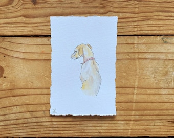 May include: Watercolor painting of a dog in profile, with a light yellow coat and a pink collar. The artwork is on a textured, rectangular piece of paper with torn edges. The background is a wooden surface.