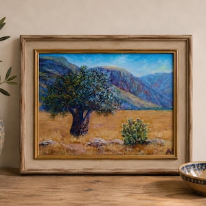 Puede incluir: Un cuadro de paisaje enmarcado que muestra un gran árbol en un campo dorado con un cactus en primer plano y montañas azules al fondo. La obra está encerrada en un marco de madera clara con un borde interior fino de color dorado.