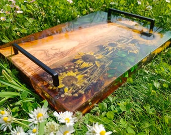 May include: A rectangular serving tray with black handles. The tray features a wooden base with dried sunflowers and other flowers encased in clear resin. The tray is set on a bed of green grass with white and yellow flowers.
