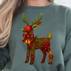 Puede incluir: Una sudadera verde azulado con un diseño de reno navideño. El reno tiene una nariz roja, cuernos verdes y dorados, y un cuerpo de retazos en rojo, verde y dorado. Presenta un lazo rojo con campanas doradas y lazos rojos en las patas.