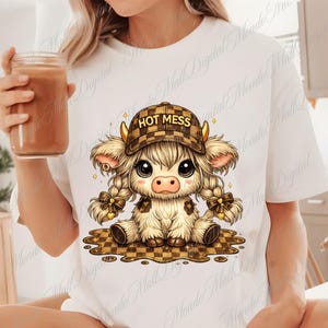 May include: White t-shirt featuring a cartoon cow with a plaid hat that reads "HOT MESS." The cow has long, braided hair and is sitting on a checkered surface. The cow is light brown and white with large eyes.